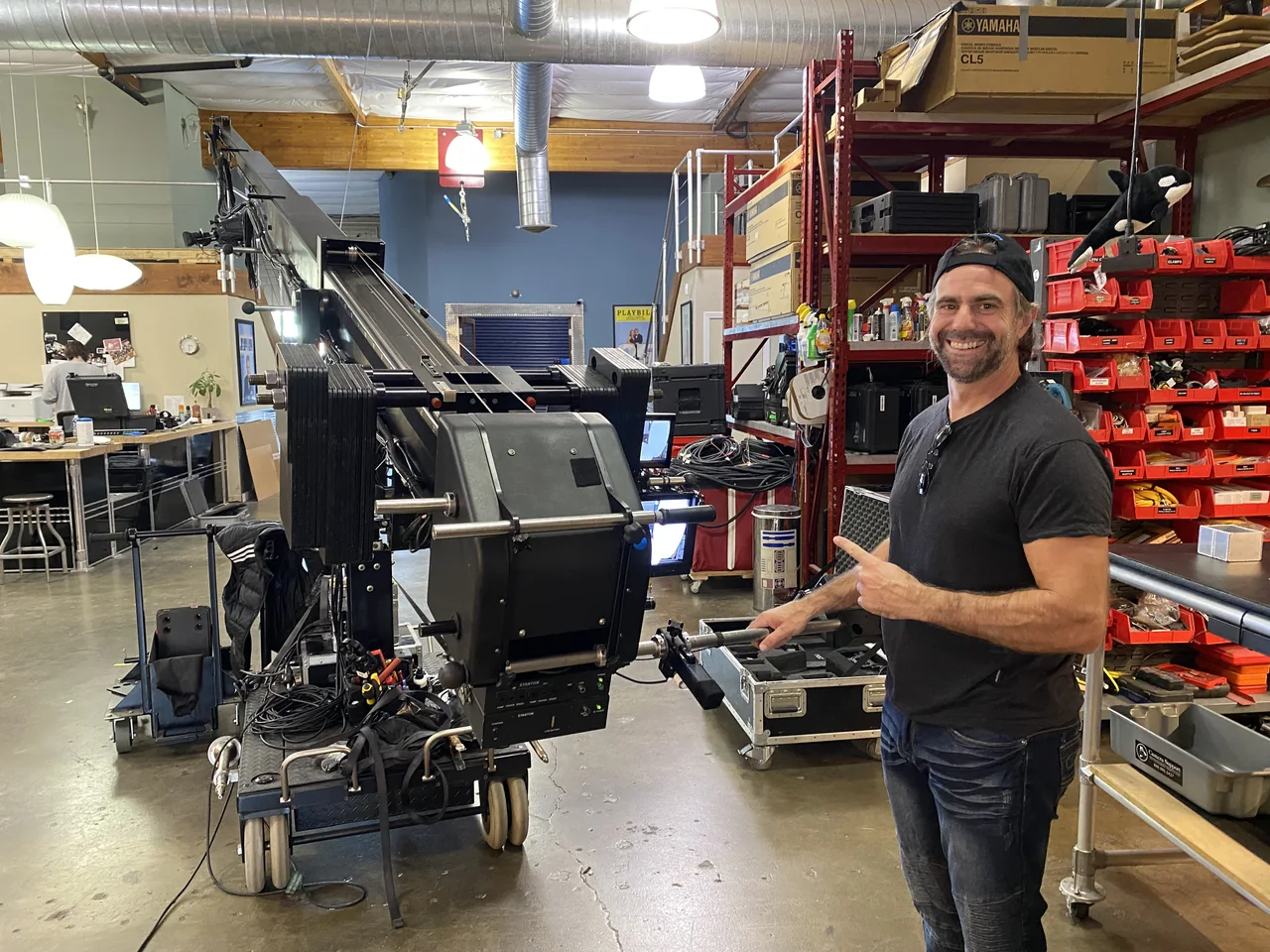 Ariel Roncoli standing beside a professional camera crane in the RA Productions equipment shop